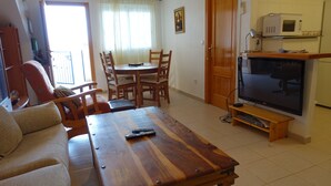 A living room with a wooden coffee table, a sofa, a TV, and a dining area with chairs and a table.