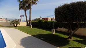 A pool area with a tiled deck, a well-maintained lawn, and a hedge.