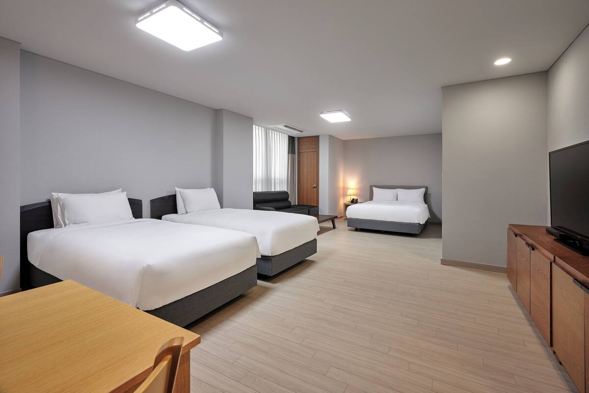 Una habitación de hotel moderna con dos camas, un escritorio de madera, un televisor y un ventanal con cortinas.
