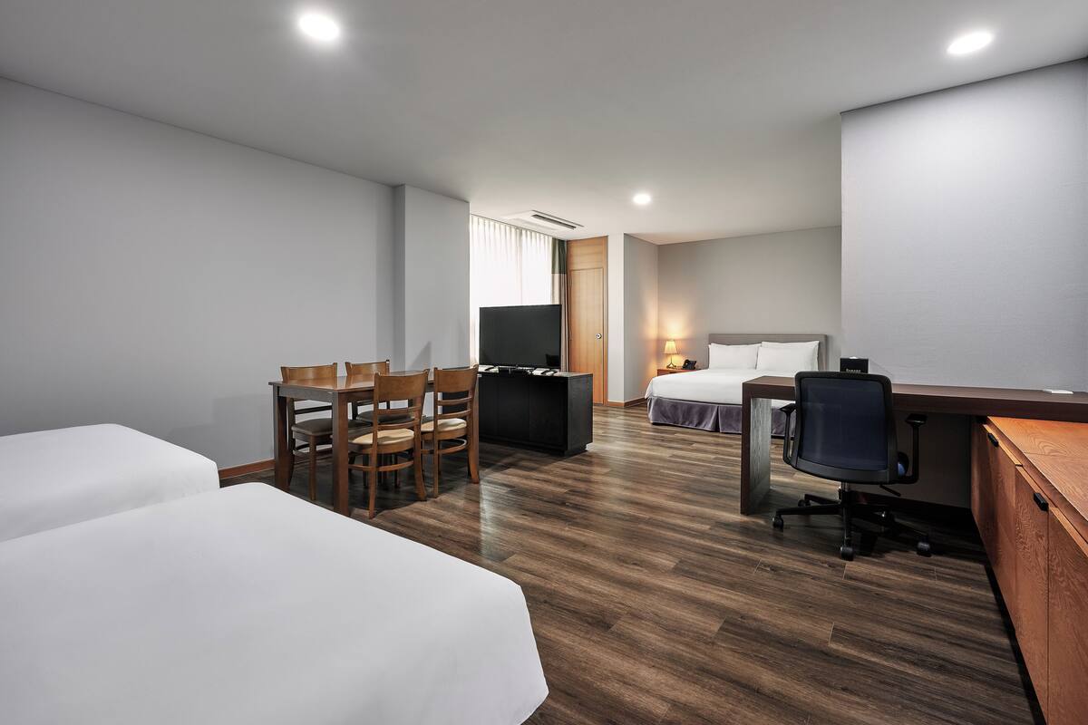 Habitación de hotel con dos camas, un escritorio, una silla, un televisor y una mesita de noche.
