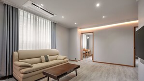 A modern living room with a beige sofa, a wooden coffee table, and a dining area visible through an open door. - Ramada Hotels & Suites Seoul Namdaemun (Seoul)