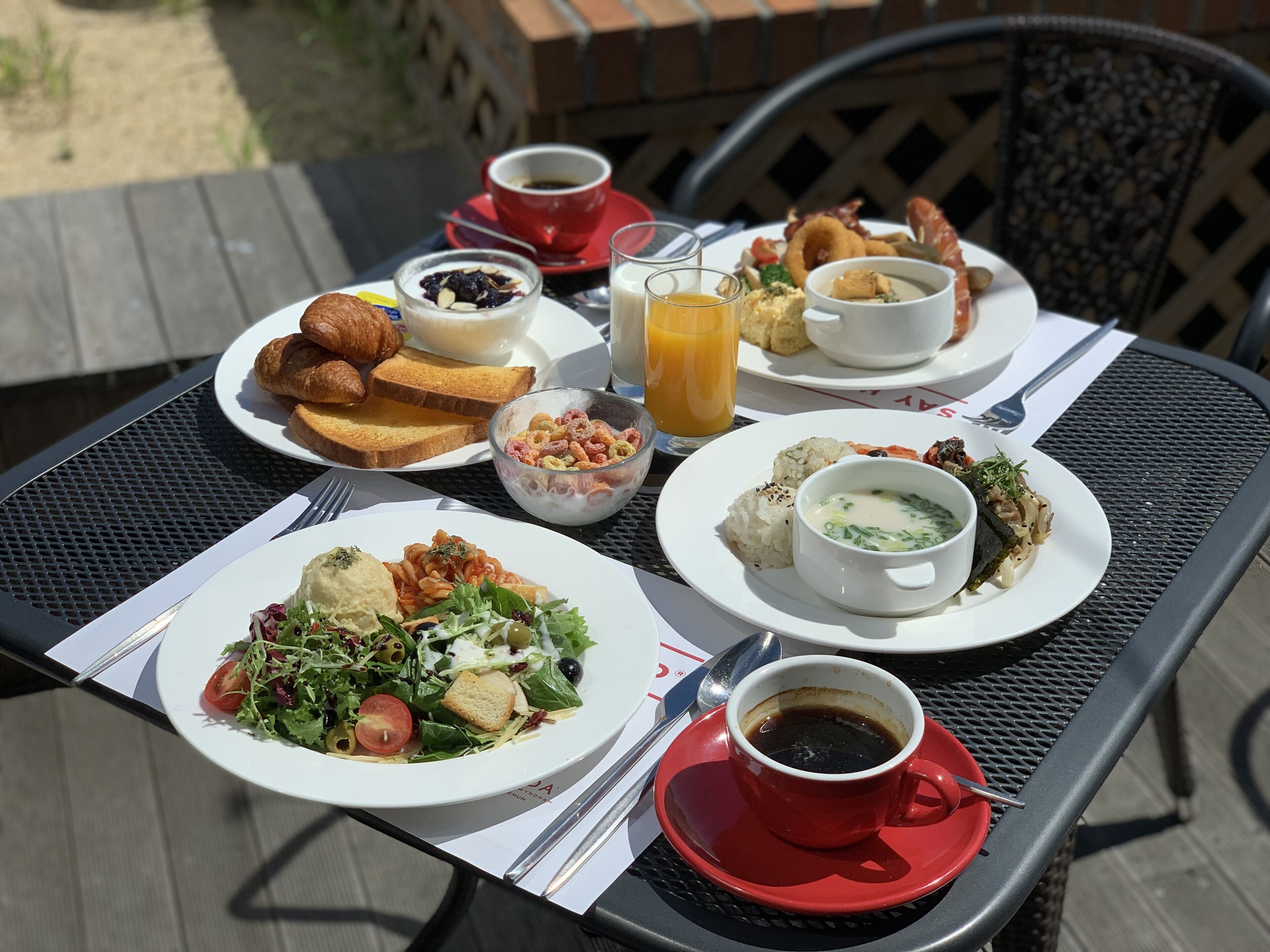 A table set with breakfast items including croissants, toast, cereal, rice balls, soup, and a salad.