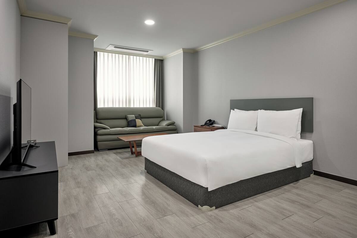 Una habitación de hotel moderna con cama, sofá, televisor y escritorio.