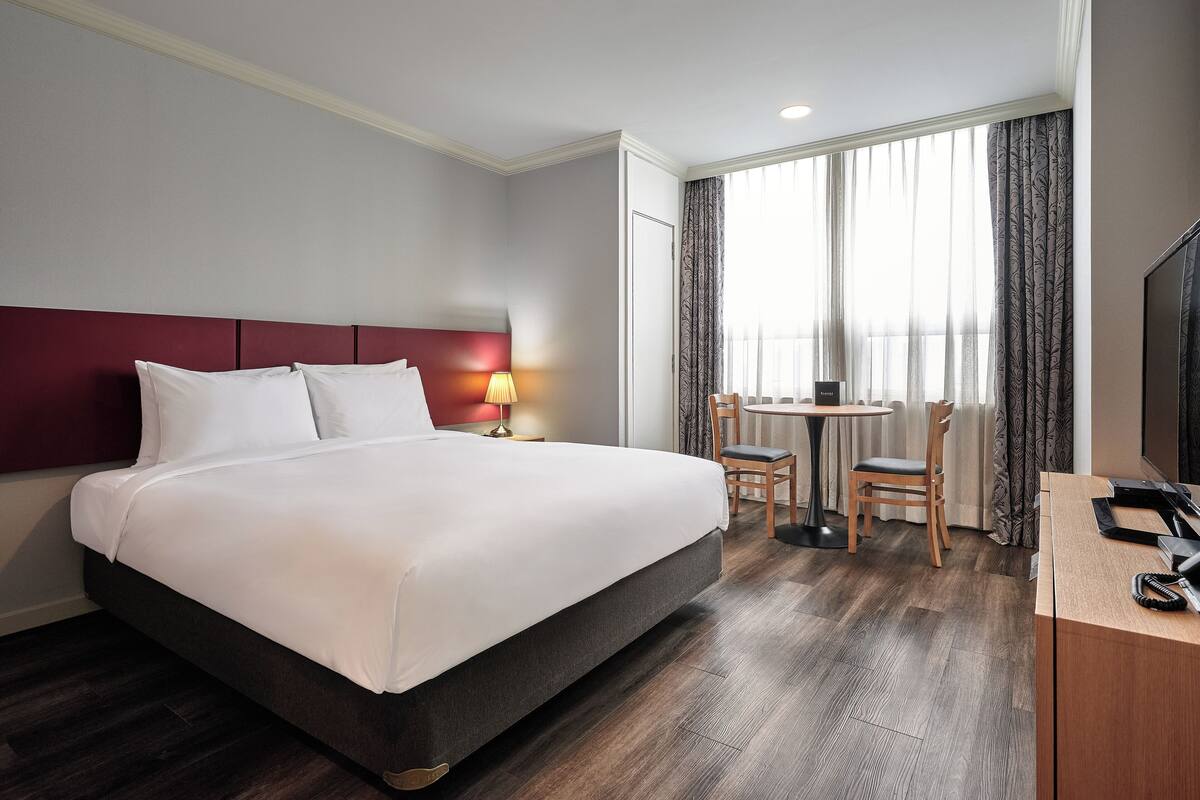 Habitación de hotel con una cama grande, un escritorio con silla, televisión y ventana con cortinas.