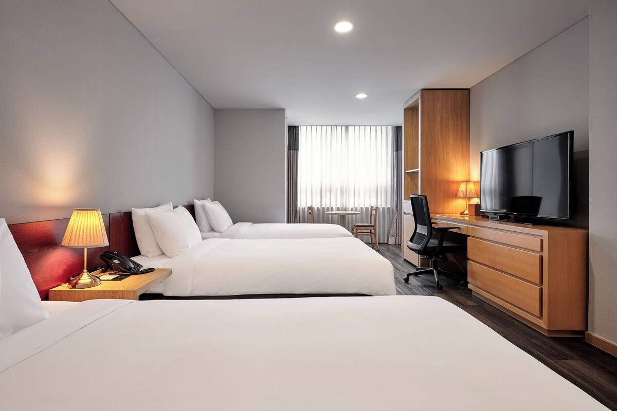 Habitación de hotel con dos camas, un escritorio, un televisor y una lámpara.