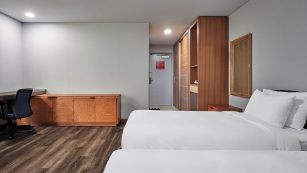 Una habitación de hotel con cama, escritorio, silla, armario y espejo.