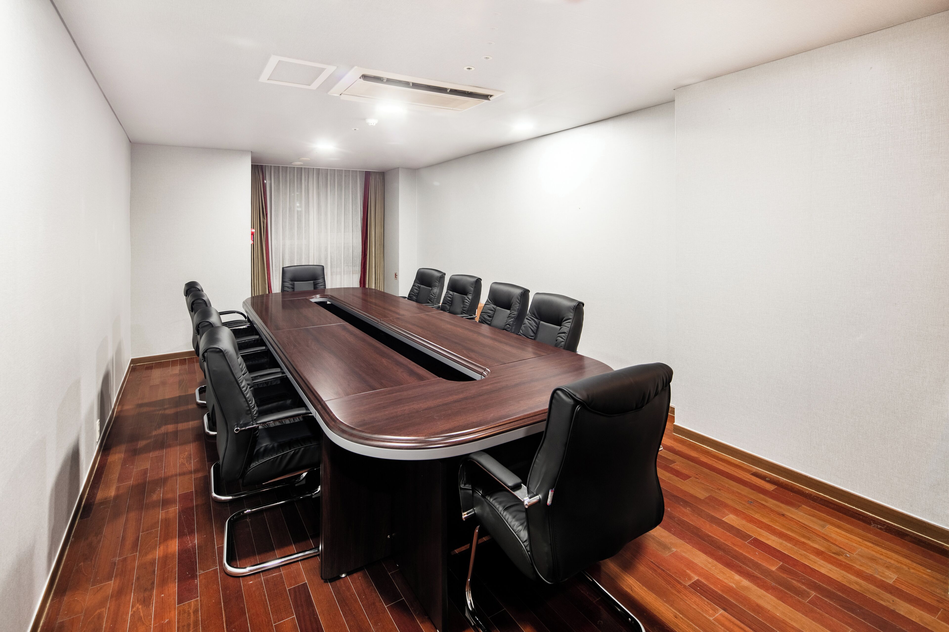 A conference room with a long table, black leather chairs, and wooden flooring.