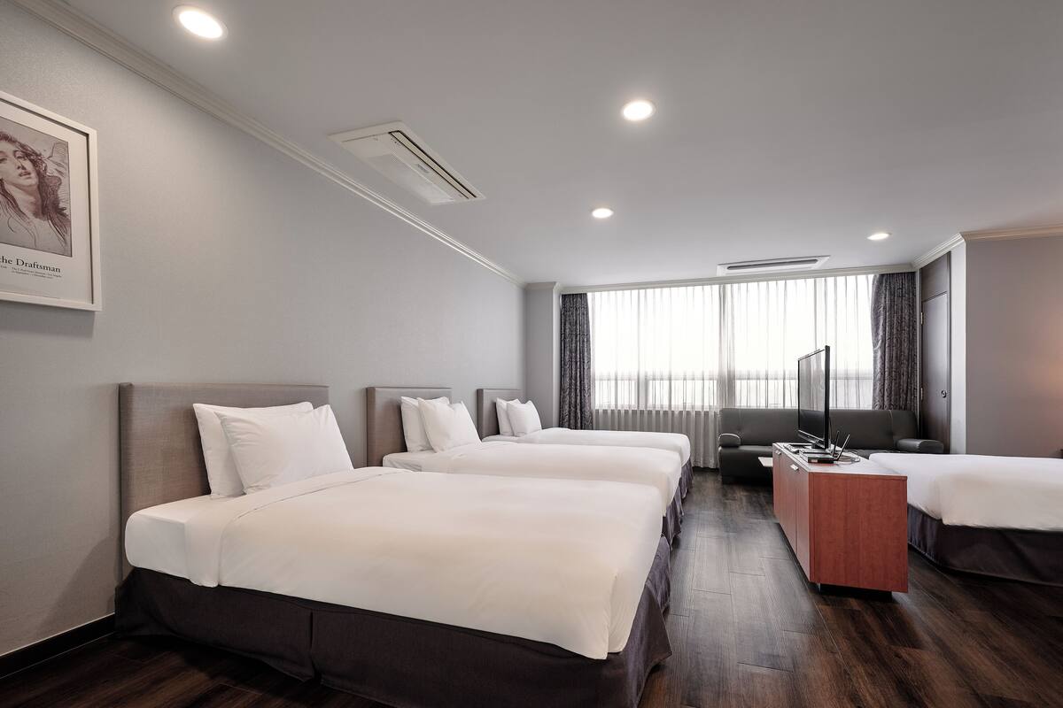 Habitación de hotel con tres camas, un escritorio y un amplio ventanal con cortinas.