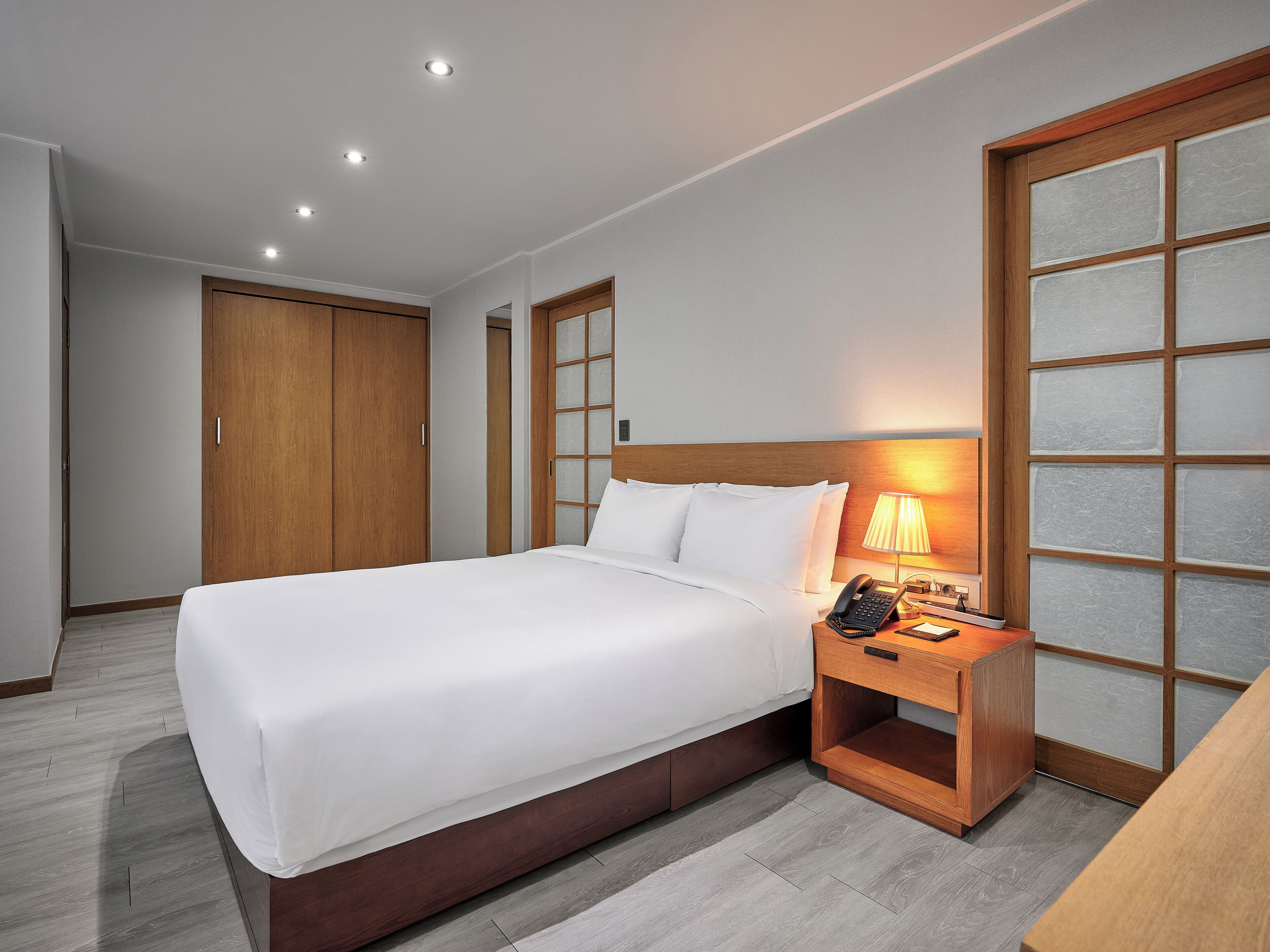 A hotel room with a large bed, a wooden nightstand with a lamp, and a wardrobe.