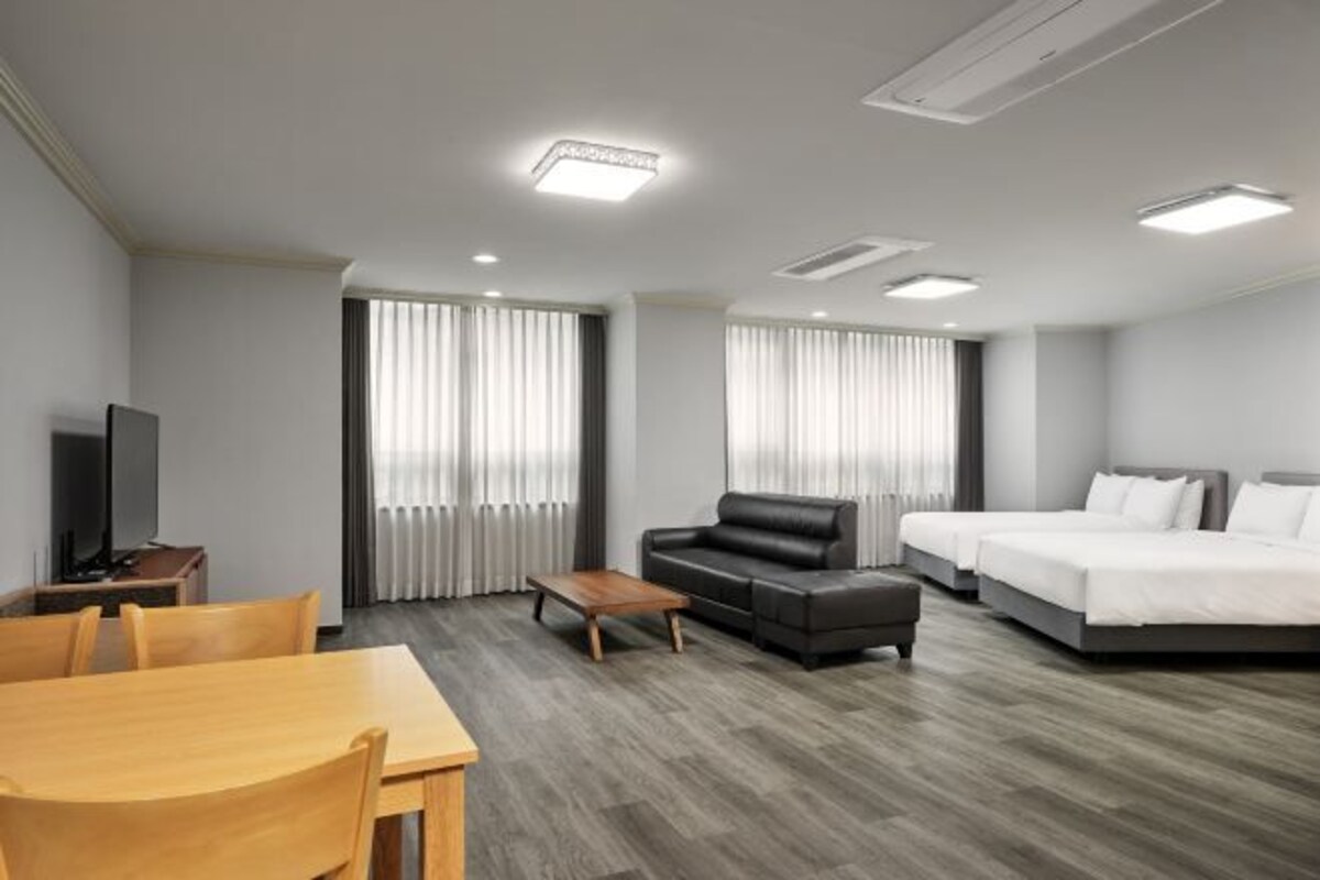 Una habitación de hotel moderna con una mesa de comedor de madera, un sofá, una cama y un televisor.