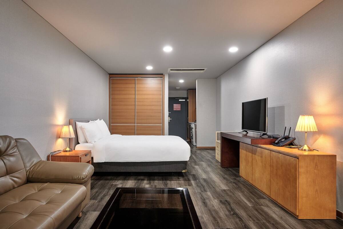 Una habitación de hotel con cama, escritorio, televisor y sofá.