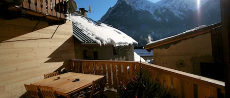 A wooden balcony with a table and chairs, a Christmas tree, and a mountain view.