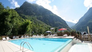 A swimming pool with lounge chairs and umbrellas, surrounded by a wooden fence, with mountains in the background.