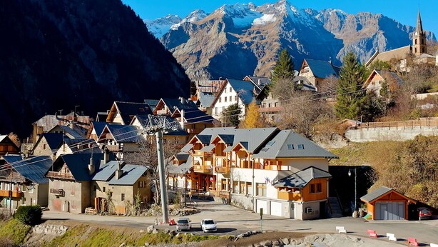 A mountain village with traditional wooden houses, a church, and a view of snow-capped mountains.