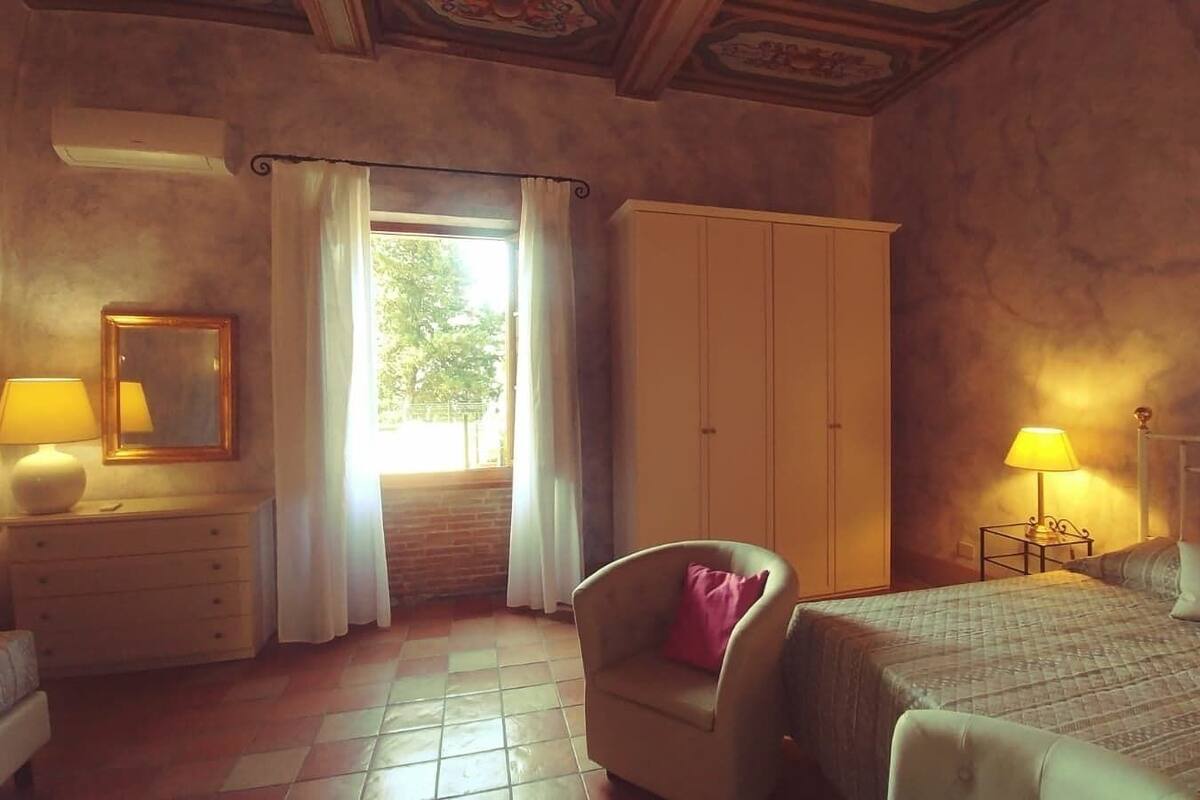 A bedroom with a bed, two bedside tables with lamps, a chair, a wardrobe, and a window with curtains.