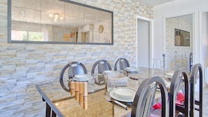 Un comedor con pared de piedra, un espejo grande y una mesa moderna lista para cuatro personas.