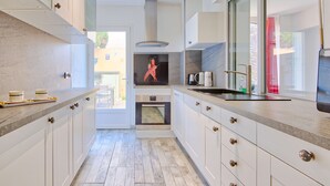 Una cocina moderna con armarios blancos, horno empotrado y un amplio ventanal.