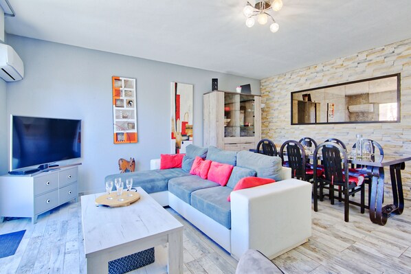 A modern living room with a sectional sofa, dining table, chairs, and a flat-screen TV.