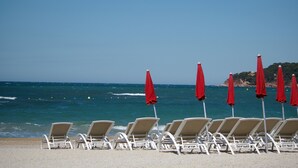 Una playa con hileras de sillas de playa blancas y sombrillas rojas.