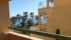 A balcony with a table set for dining, overlooking a coastal area with palm trees and a view of the sea. - PORTISSOL T2 TERRACES SEA VIEW 100M BEACH (Sanary-sur-Mer)