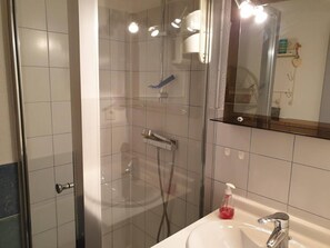 Casa de banho moderna com cabine de duche em vidro, lavatório branco e espelho em cima.