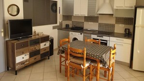 A compact kitchen with a dining table, wooden chairs, a television, and a washing machine. - PORTISSOL T2 TERRACES SEA VIEW 100M BEACH (Sanary-sur-Mer)