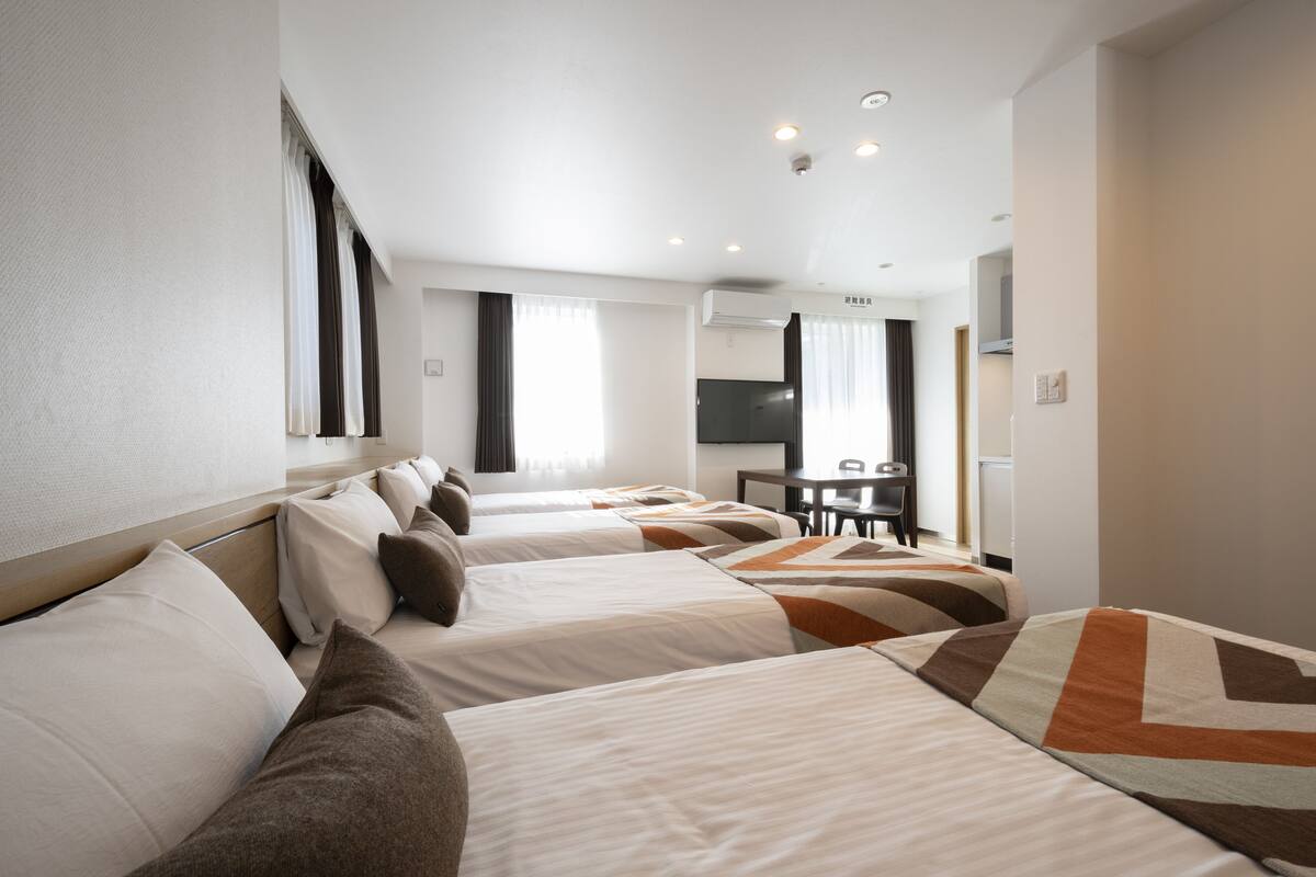 A hotel room with four beds, a desk, and a television.