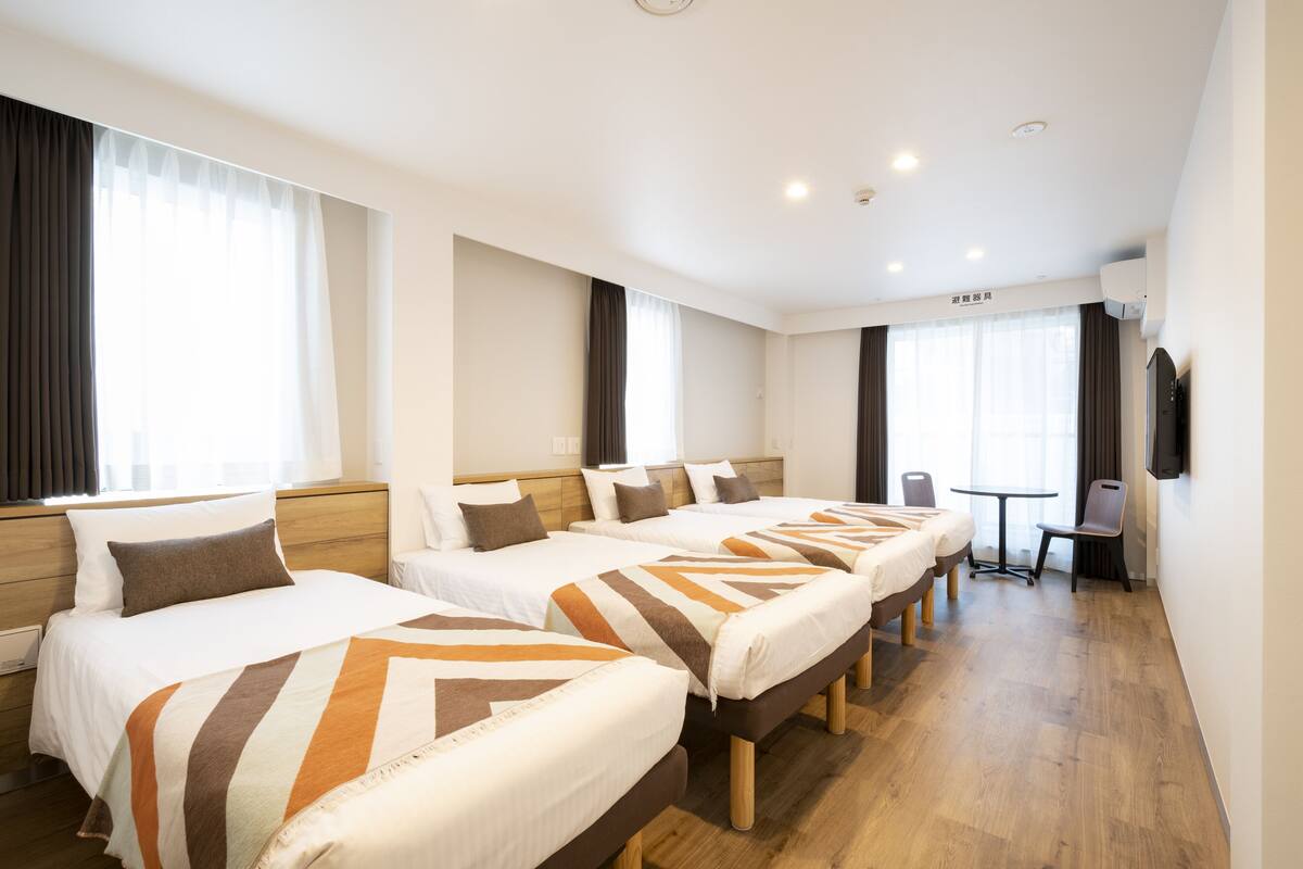 A hotel room with three beds, a small table, and a TV.