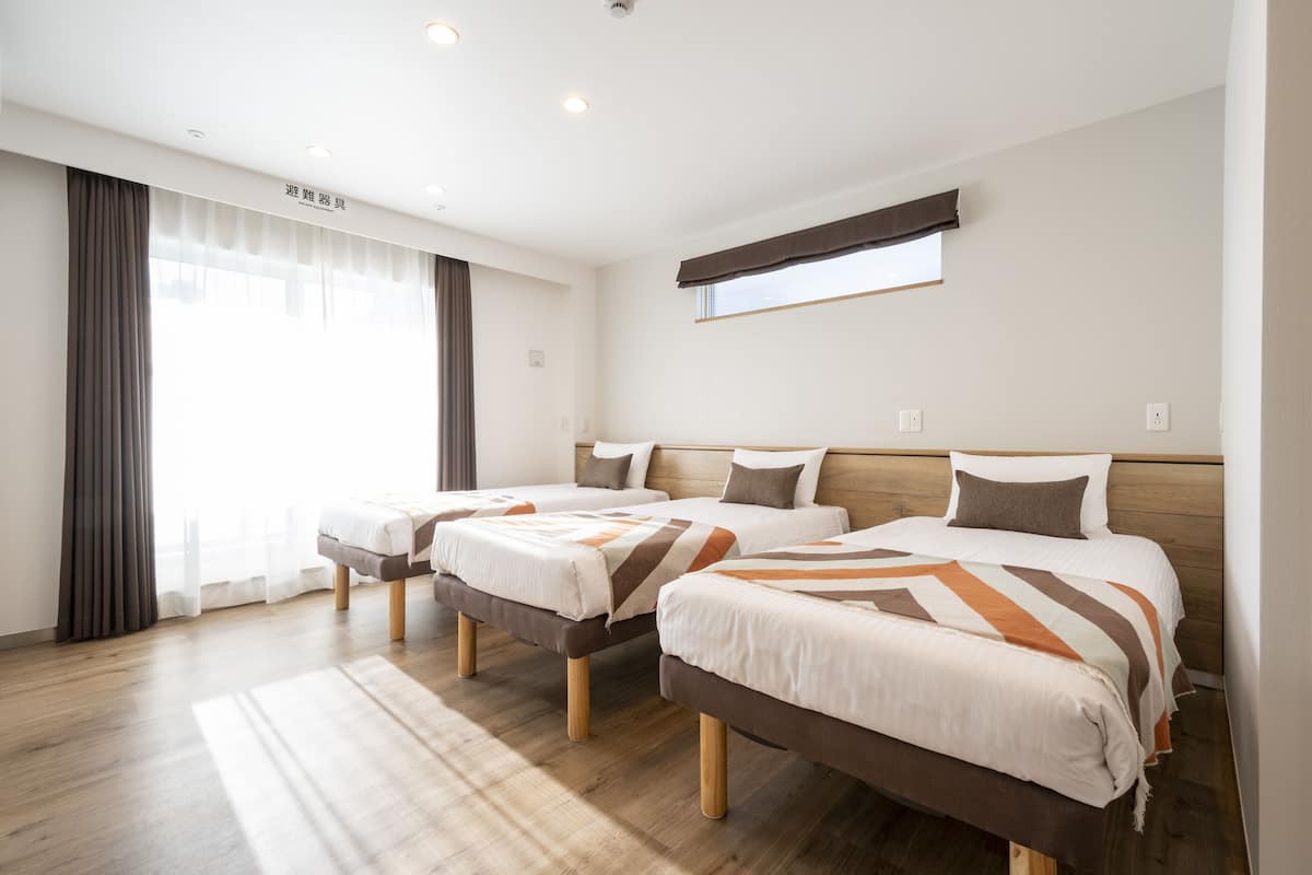 A hotel room with two beds, wooden headboards, a large window with curtains, and a wooden floor.