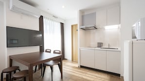 Una cocina moderna con comedor, armarios blancos, microondas integrado y televisor de pantalla plana.