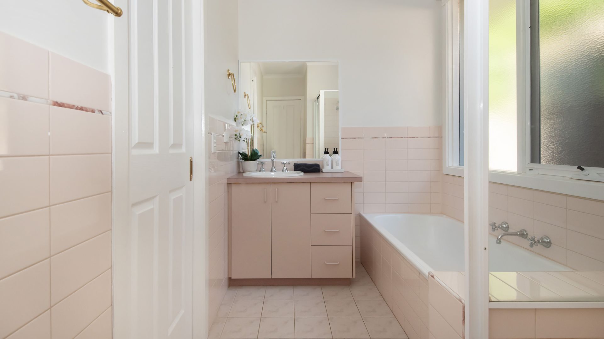 A bathroom with a white sink, a mirror, a bathtub, and a door leading to another room.
