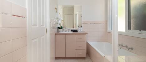 A bathroom with a white sink, a mirror, a bathtub, and a door leading to another room.