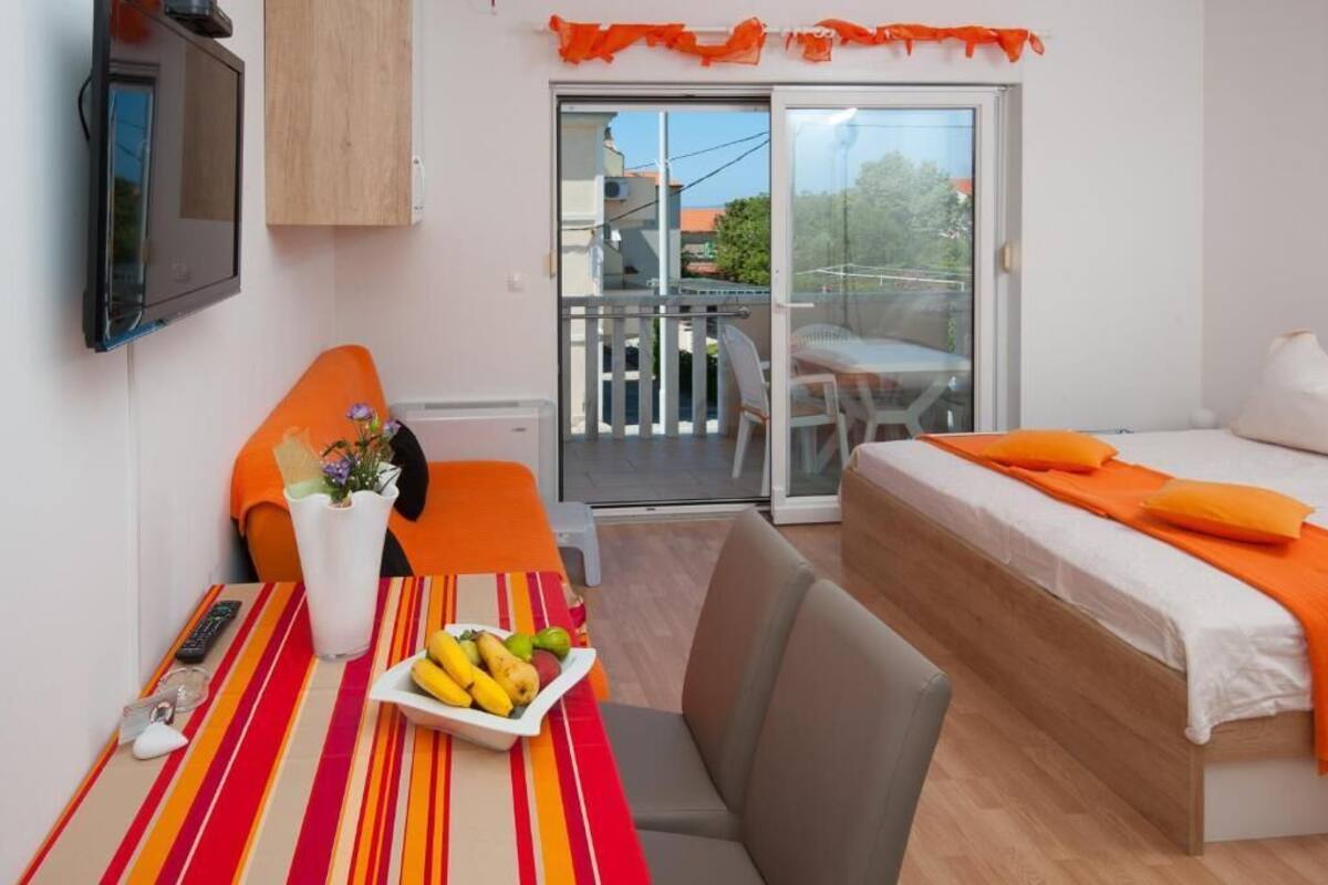 A hotel room with a bed, a dining table with fruit, a TV, and a balcony with a view.