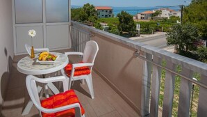 Ein Balkon mit Tisch und Stühlen, eine Vase mit einer Blume und Blick auf das Meer und Gebäude.
