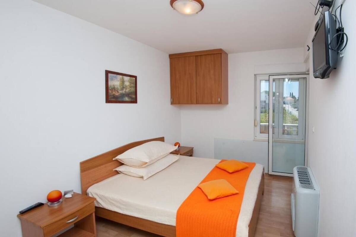 A bedroom with a bed, a nightstand, a television, a window, and a door.