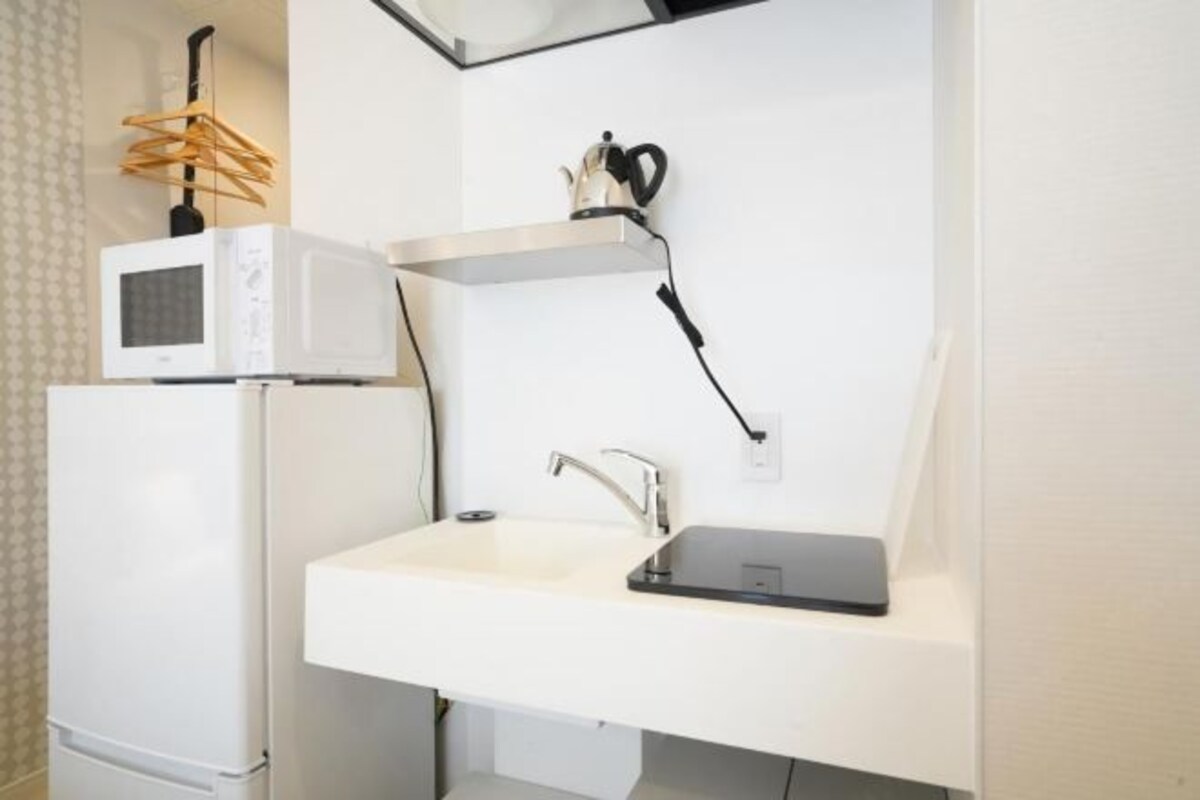 A modern bathroom with a white sink, a built-in microwave, and a kettle on a shelf.