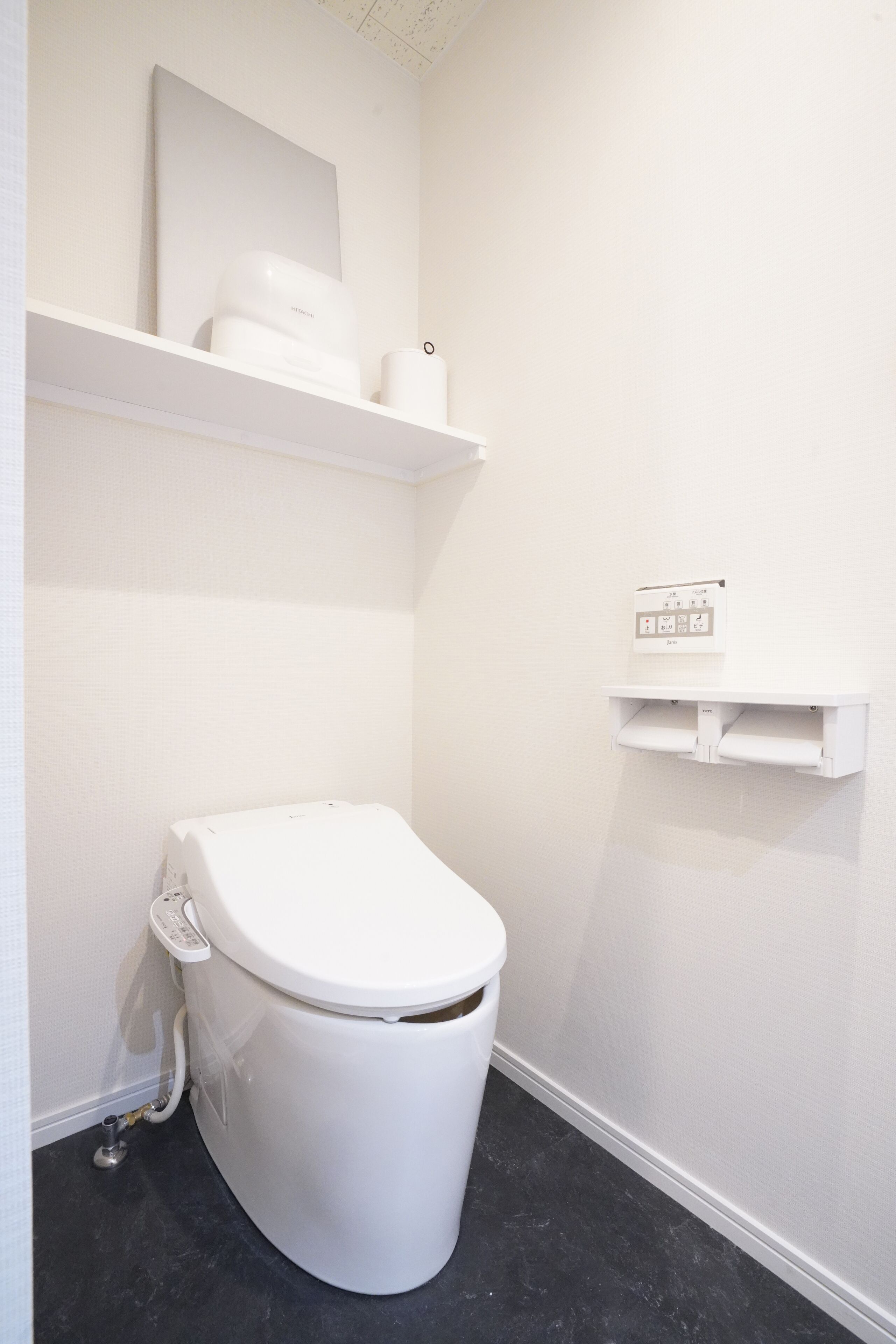 Un baño pequeño y blanco con un inodoro, un estante sobre el inodoro y un enchufe en la pared.