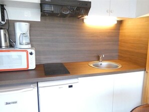 Uma cozinha compacta com micro-ondas, cafeteira e pia.