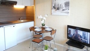 A modern kitchen with white cabinets, a wooden countertop, a dining table with chairs, a vase with flowers, and a television on a stand. - Cozy studio for 4 in Saint-Lary-Soulan with south-facing balcony (Saint-Lary-Soulan)