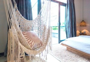 A room with a macrame hanging chair, a bed with a white headboard, and a view of the outdoors through a glass door. - Aya Homestay (Ho Chi Minh City)