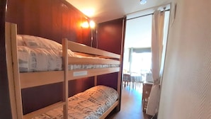 Quarto com beliche, cabeceira de madeira, uma pequena mesa e uma cadeira ao fundo.