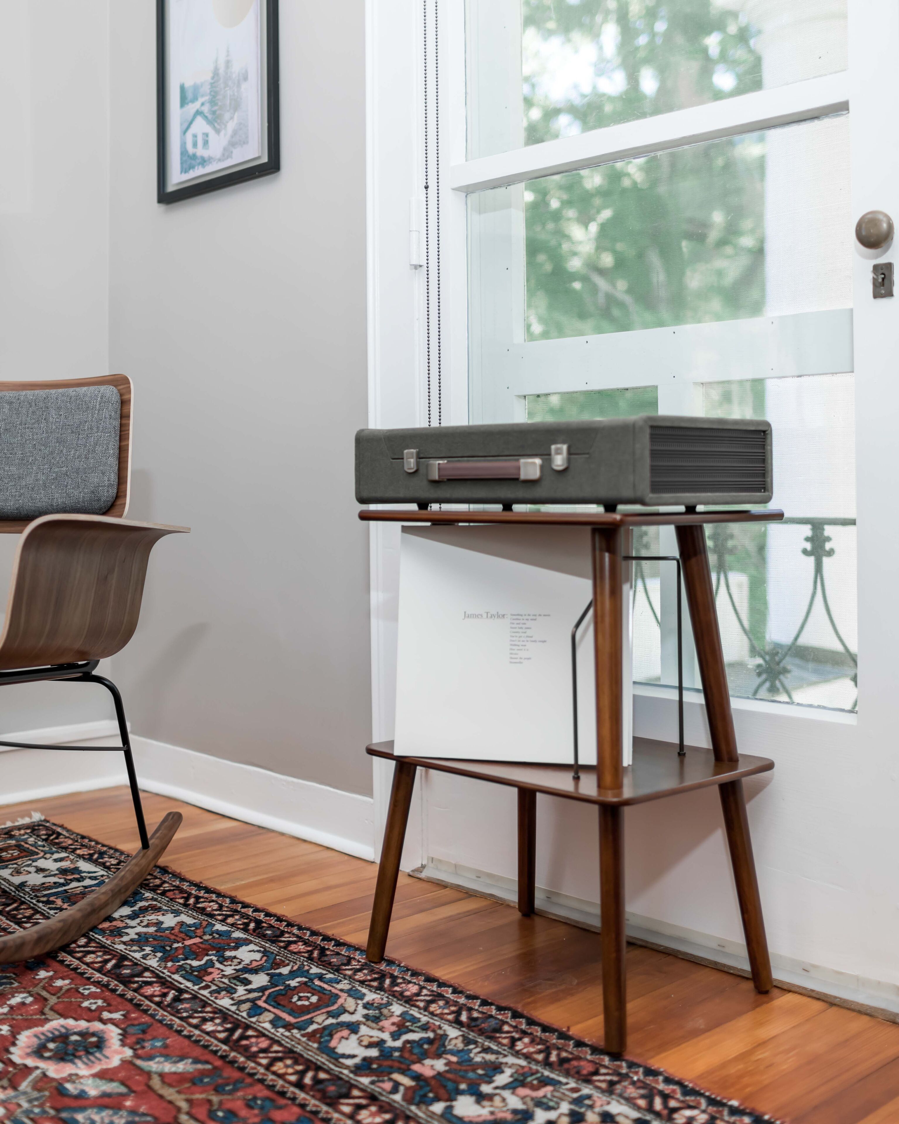 A room with a wooden floor, a patterned rug, a chair, a small table with a vintage radio, and a door with a window view.