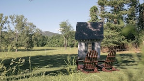 A small cabin with two Adirondack chairs in a grassy field, surrounded by trees and a mountain in the background. - Granville House (Housatonic)