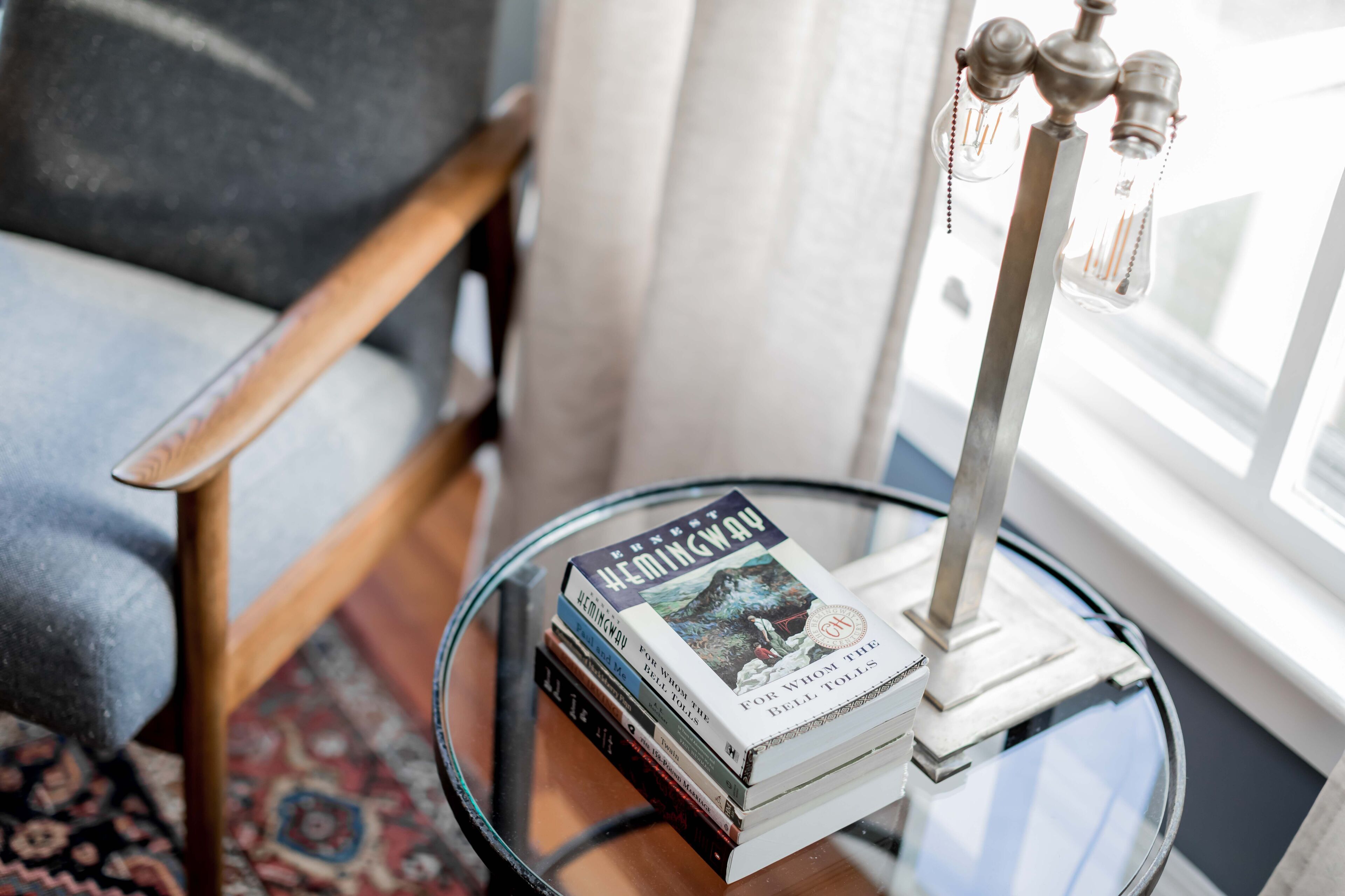 A stack of books on a glass table with a metal lamp.
