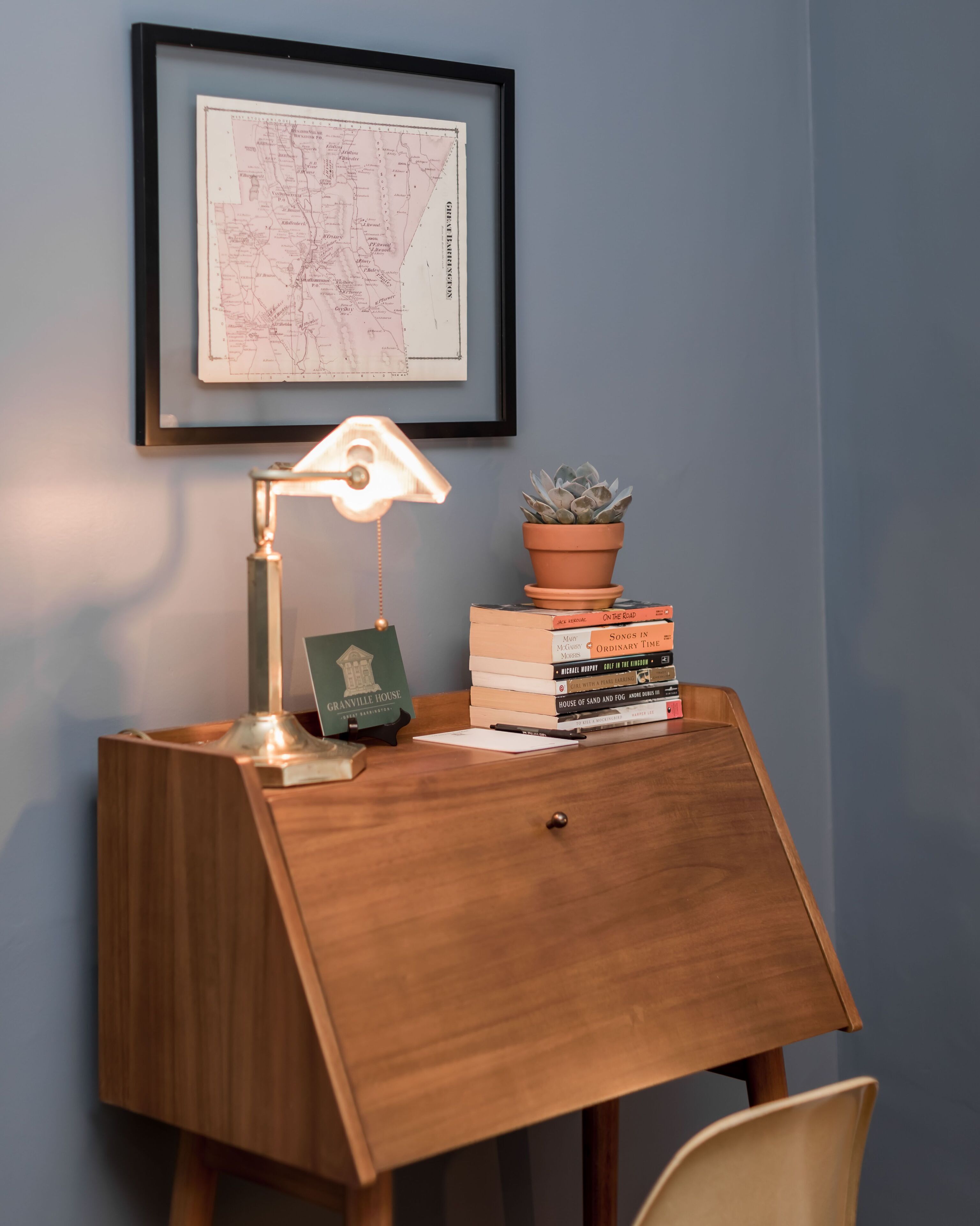 Ein Holztisch mit einer Karte, einer Schreibtischlampe, einer Topfpflanze und einem Stapel Bücher.