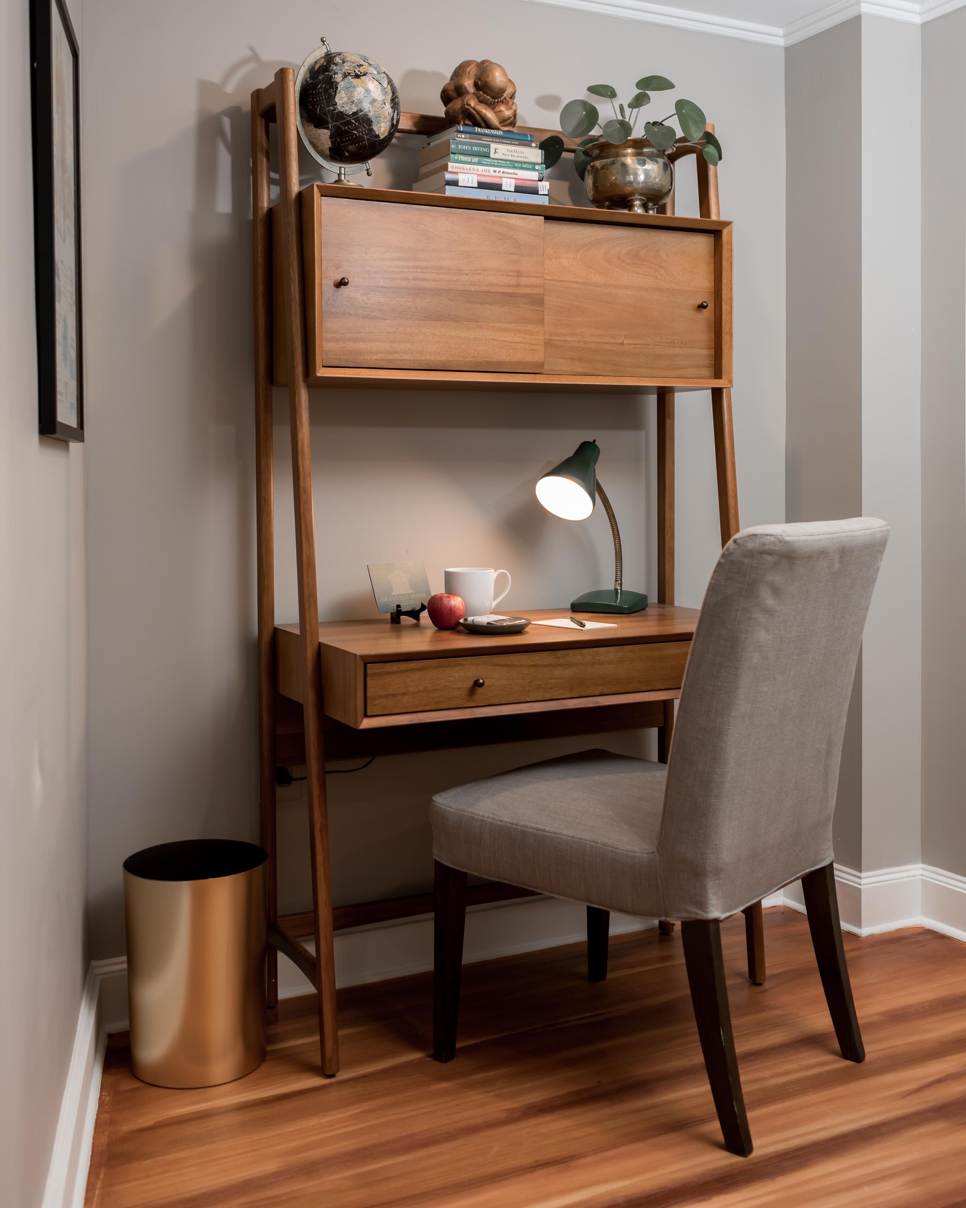 Un espacio de trabajo reducido con un escritorio de madera, una silla, un globo terráqueo, libros y una lámpara.