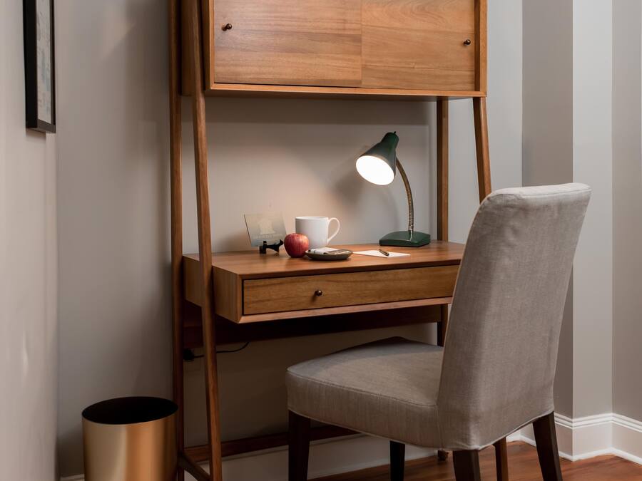 Un espacio de trabajo reducido con un escritorio de madera, una silla, un globo terráqueo, libros y una lámpara.