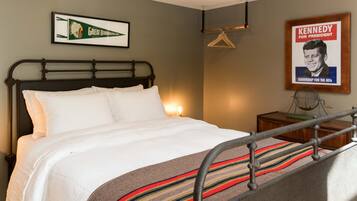 Habitación de hotel con cama, un cuadro enmarco de una campaña política, un perchero y una mesita con un ventilador.