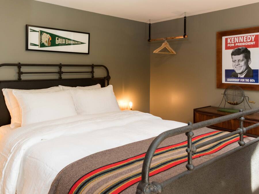 Habitación de hotel con cama, un cuadro enmarco de una campaña política, un perchero y una mesita con un ventilador.
