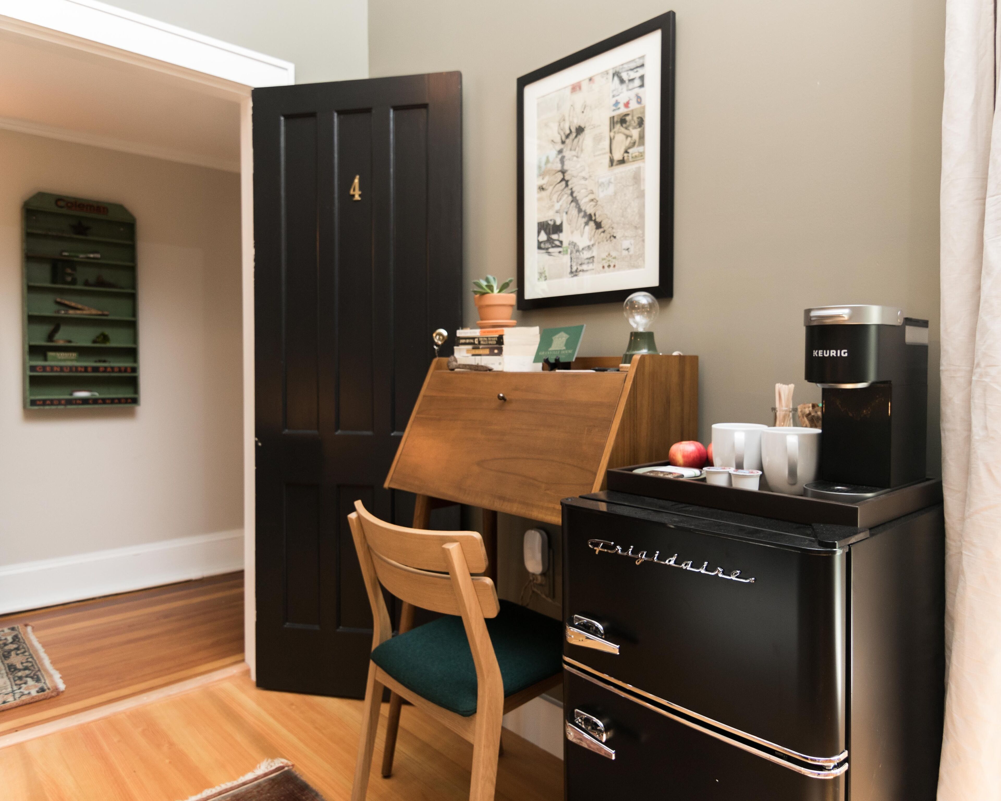A compact kitchenette with a coffee maker, a small refrigerator, and a wooden chair.
